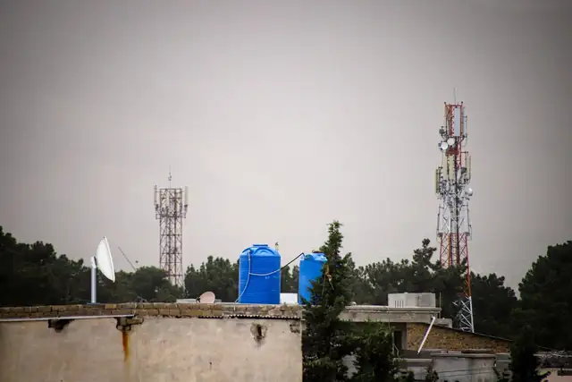 A thin lattice tower with radios on top stands behind a flat house roof. On the roof, a short pipe holds a round Mimosa C6x radio dish pointed at the tower, and a thin light line joins the two.